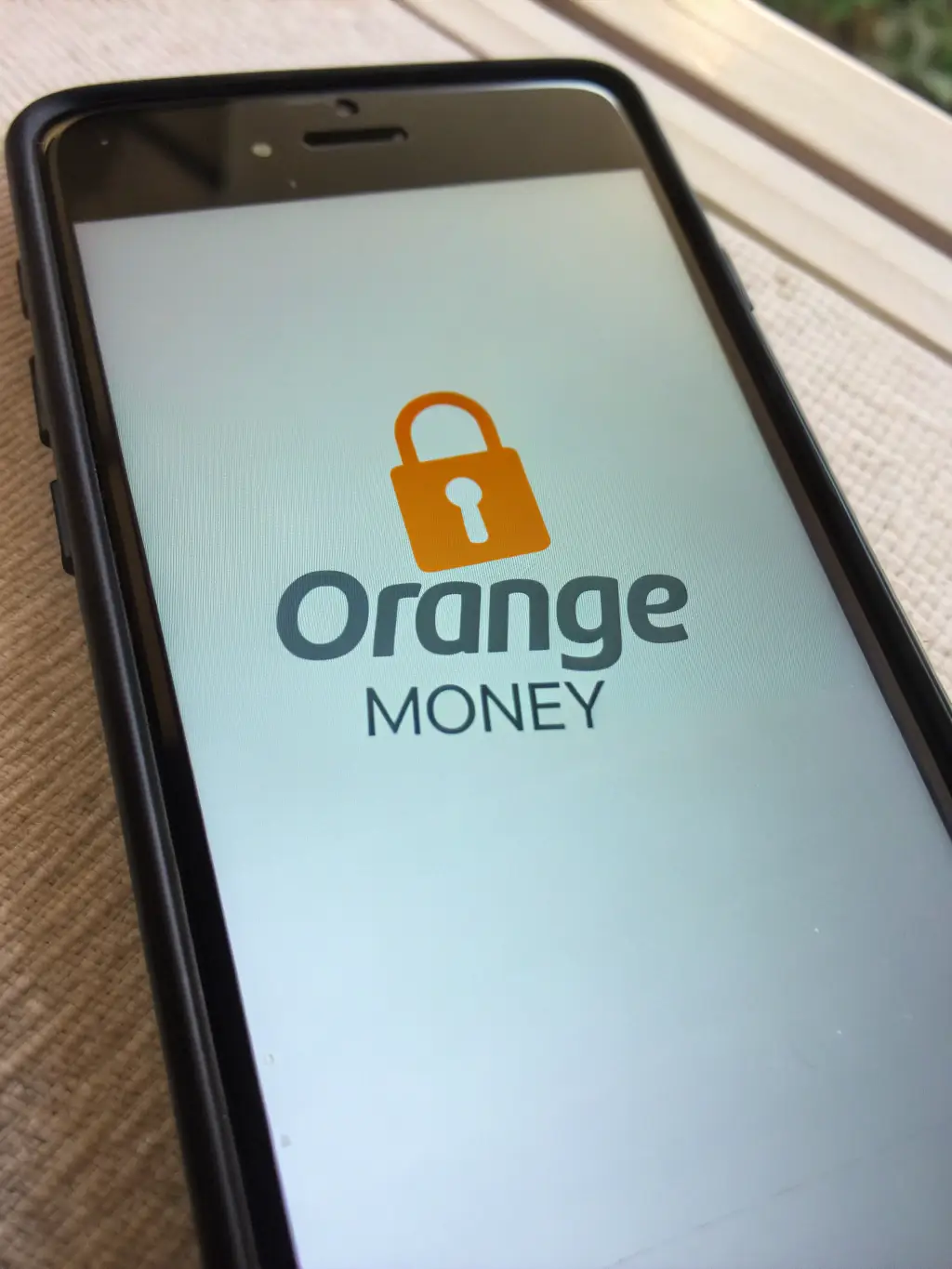 A smartphone displaying the Orange Mobile Money app interface, showing options for sending and receiving money, with the Orange logo prominently displayed. The screen features a clean layout with icons for transactions, balance, and recent activity, set against a simple background.